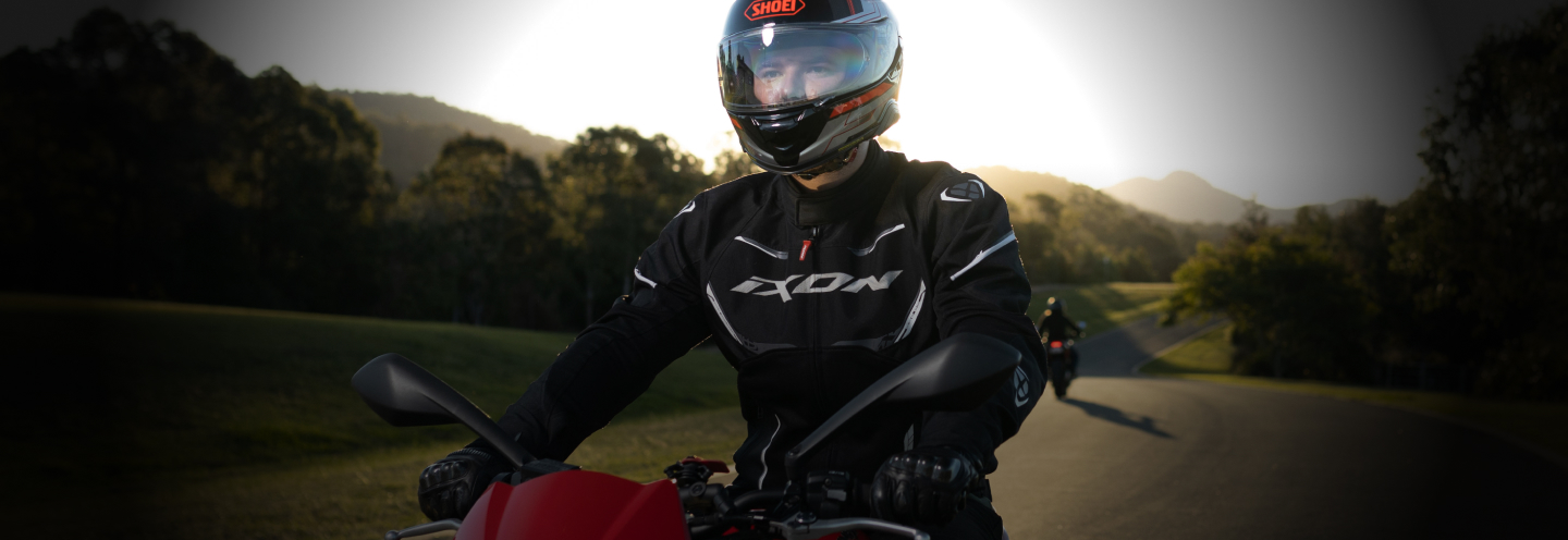 A man in full riding gear riding a motorbike in a rural area.